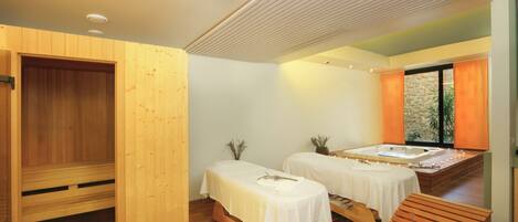 Uma sala de spa com mobiliário de madeira, duas mesas de massagem, uma banheira de hidromassagem e uma sauna de madeira.