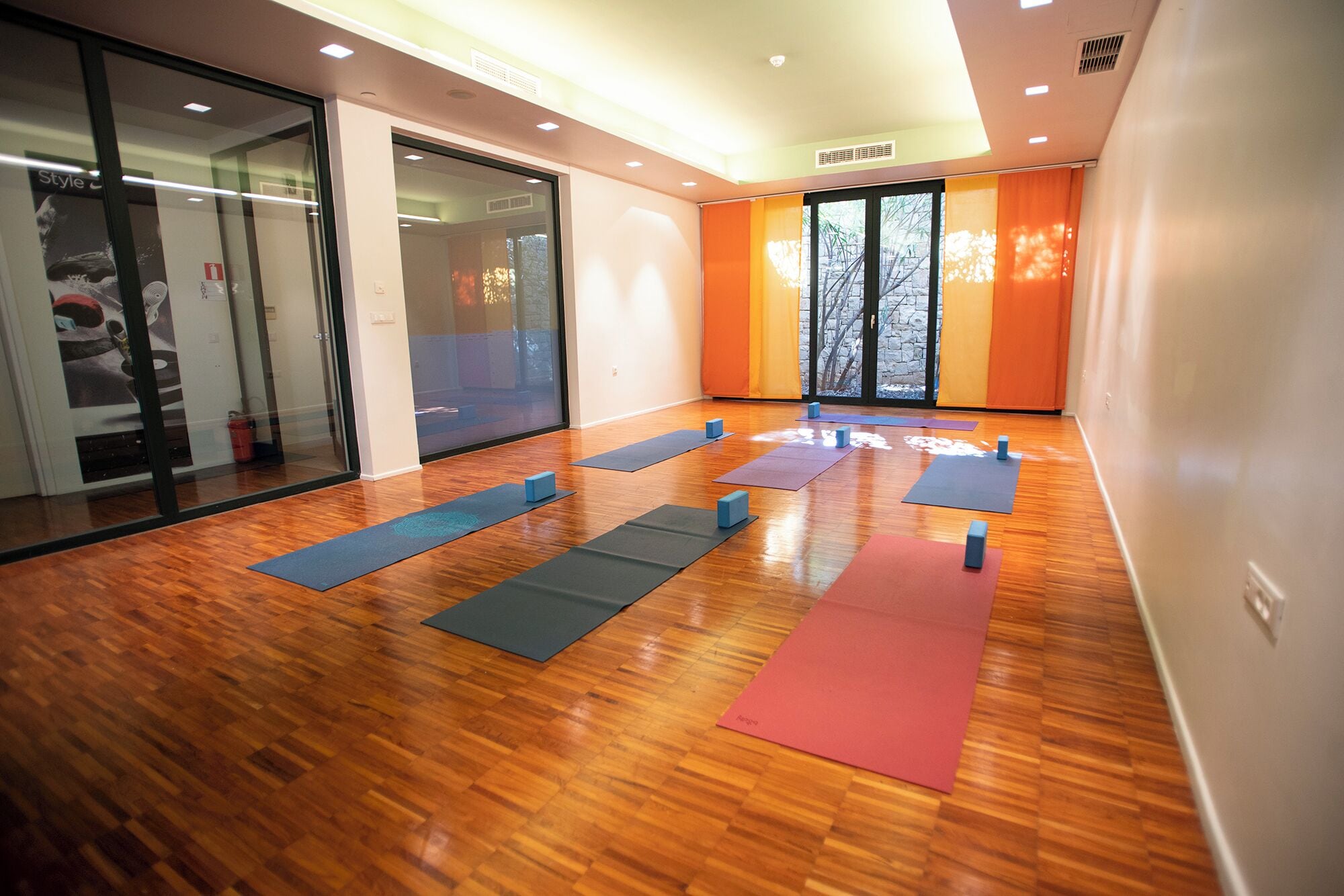 Una habitación amplia con piso de madera, ventanas grandes y colchonetas de ejercicios dispuestas para actividades físicas.