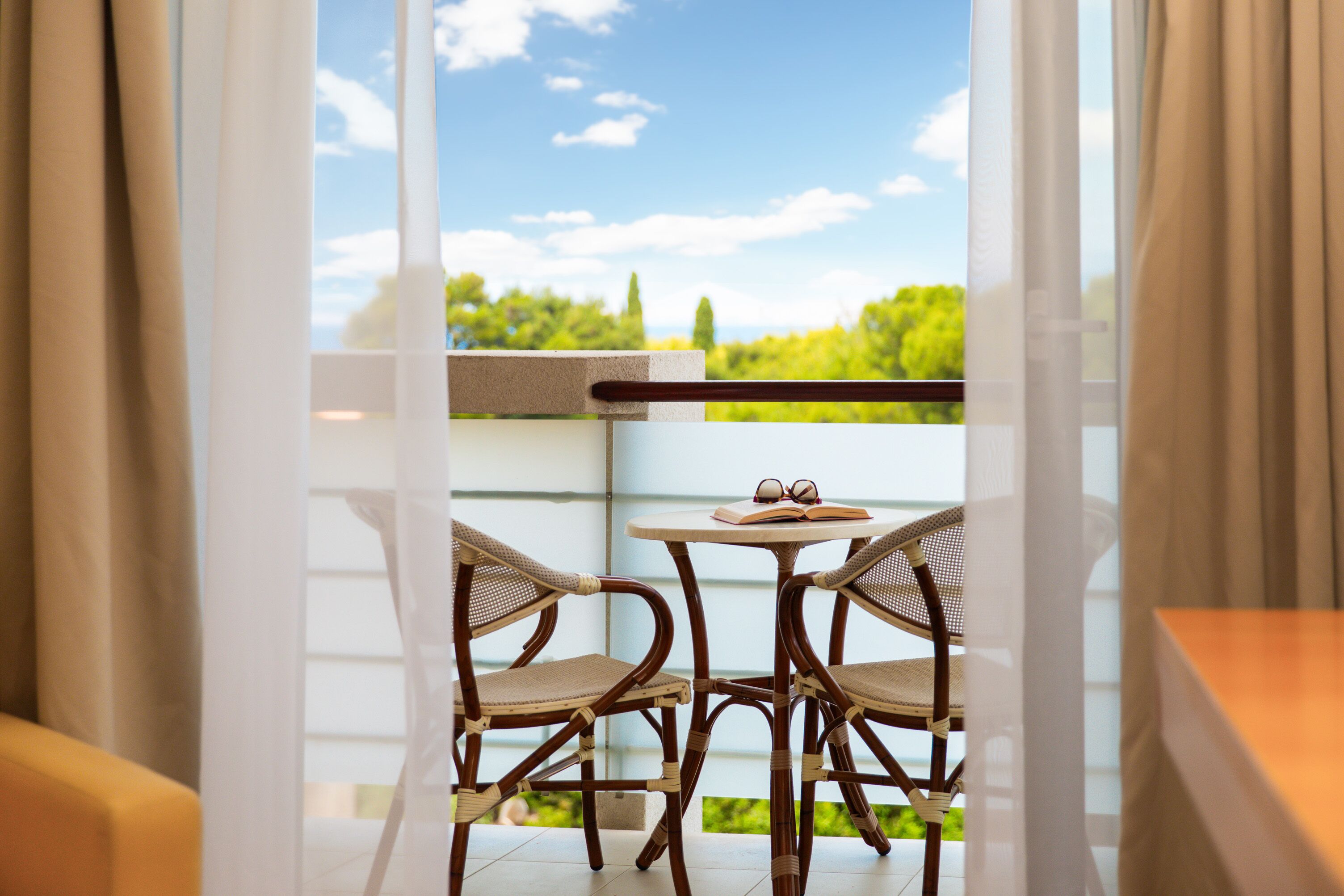 A balcony with wicker chairs, a small round table, and an open book.
