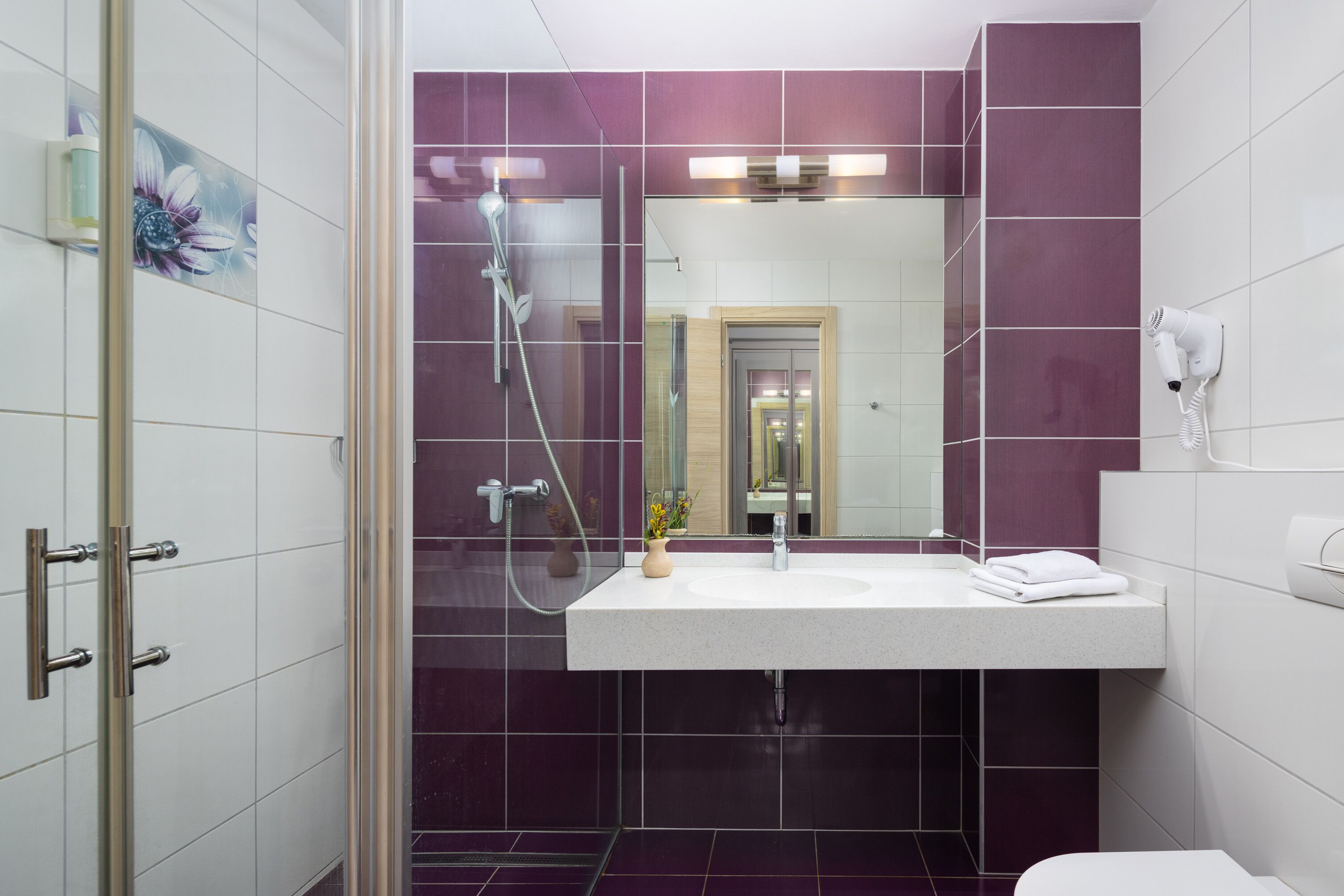 A modern bathroom with a glass shower enclosure, a white sink, and a mirror above it.