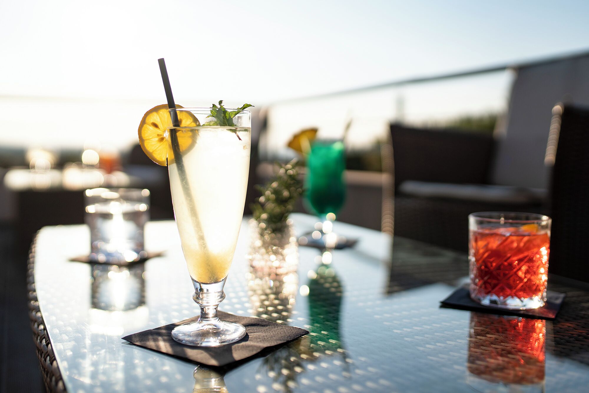 A table with three glasses of beverages, one with a lemon slice and mint, another with a red drink, and a third with a clear drink.