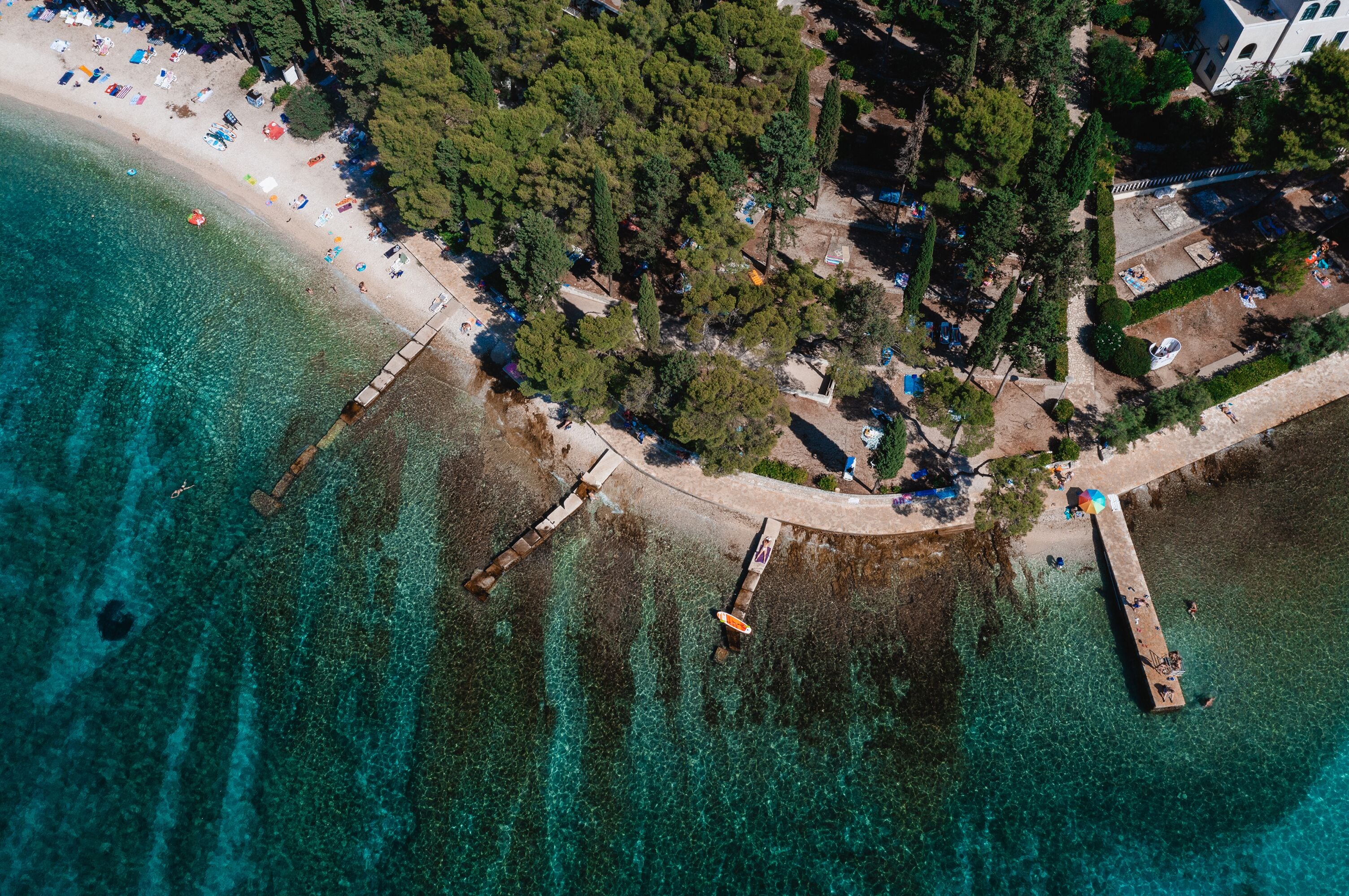 Vista aérea de uma área costeira com praia, águas turquesa cristalinas e um cais que se estende para o mar.