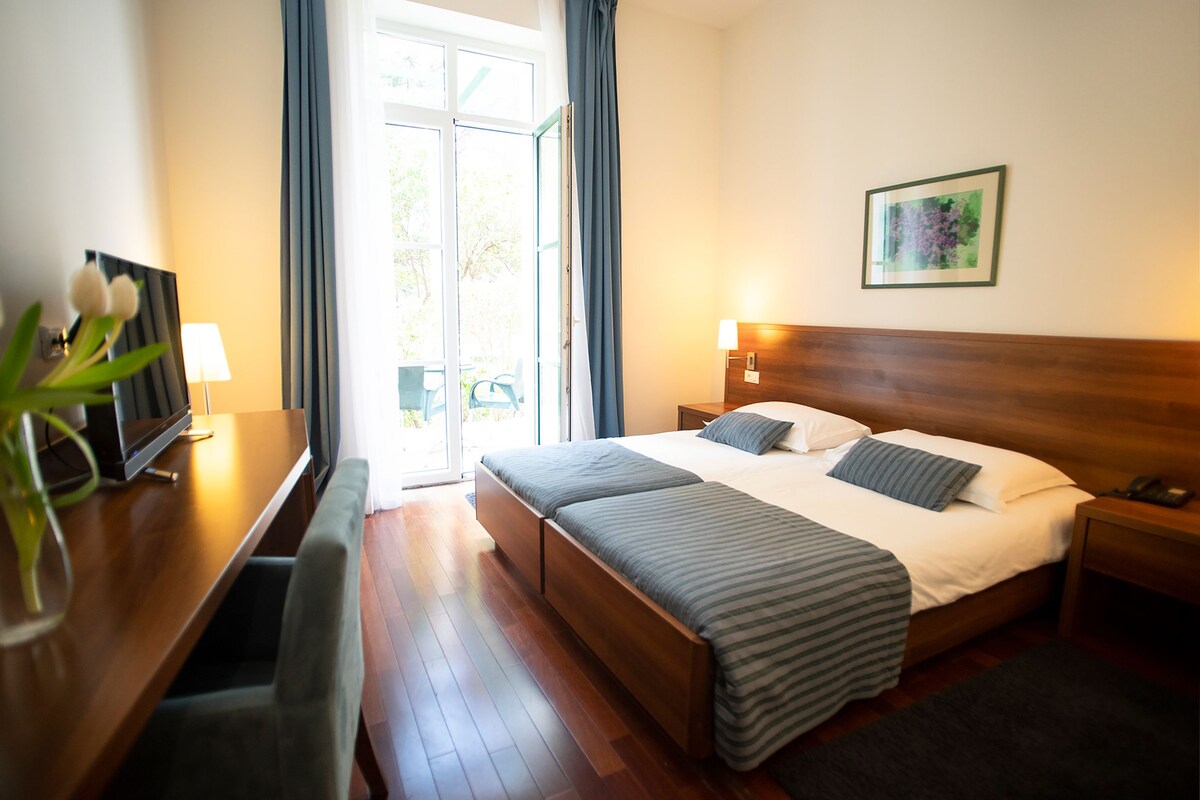 A hotel room with a bed, bedside tables, a desk, and a window.