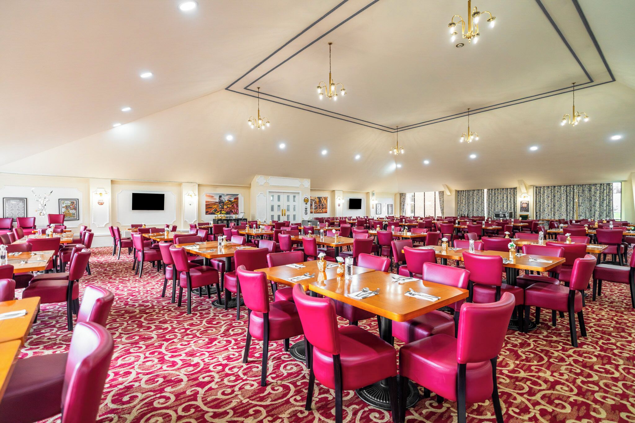 A spacious dining area with multiple tables and chairs, a patterned carpet, and ceiling lights.