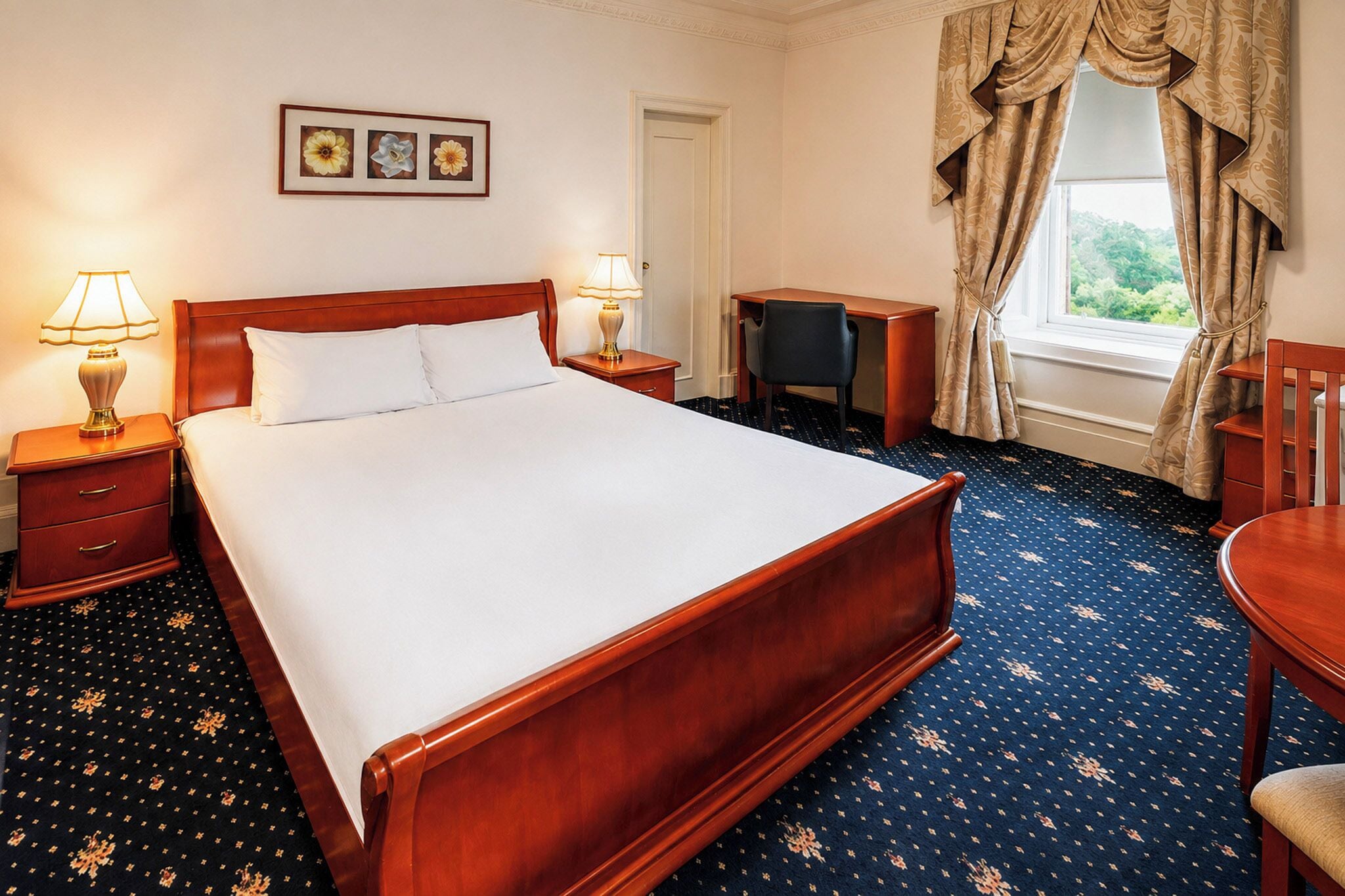 A hotel room with a large bed, two bedside tables with lamps, a desk, a chair, and a window with curtains.