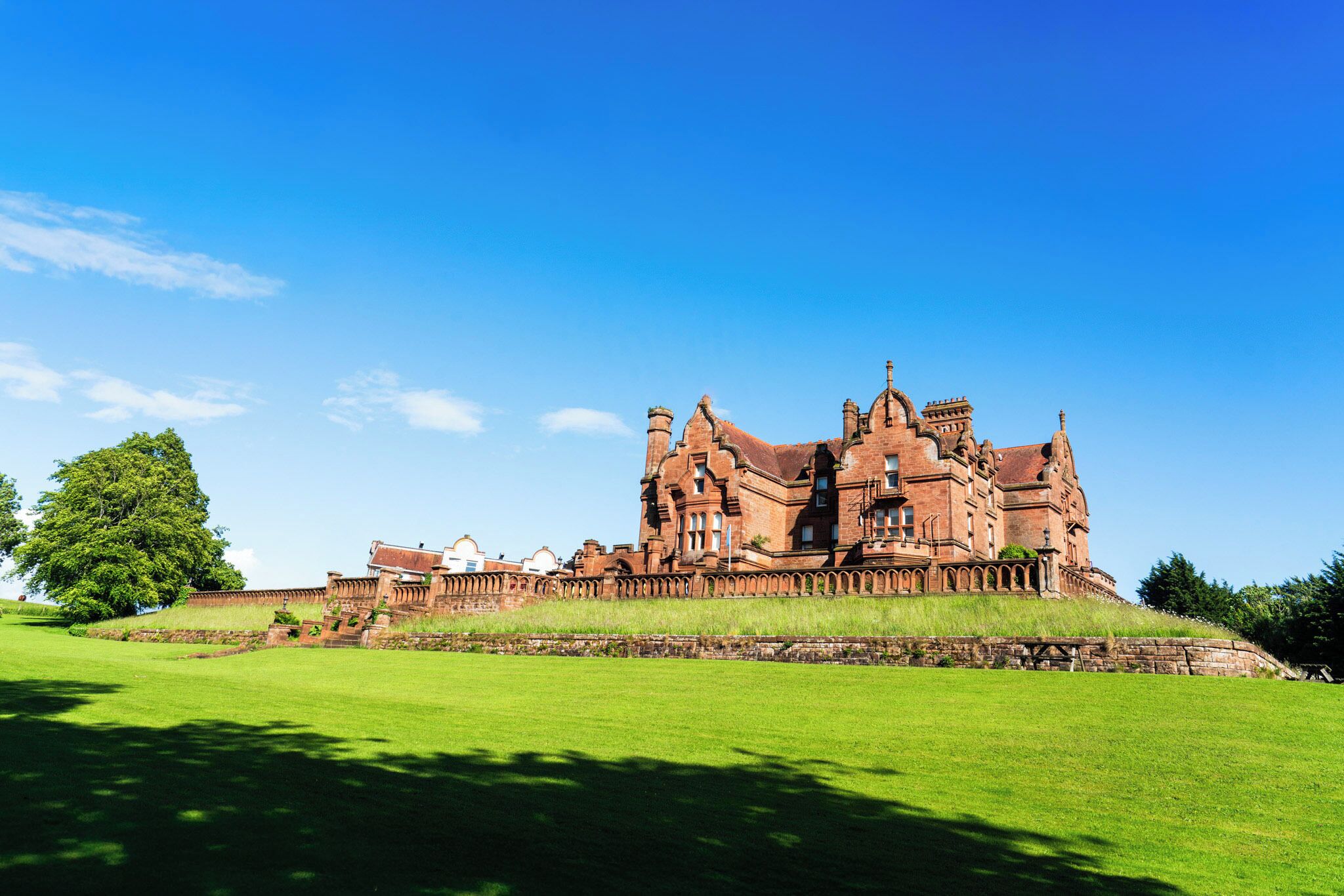 A large, historic building with multiple towers and arched windows, surrounded by a well-maintained lawn.