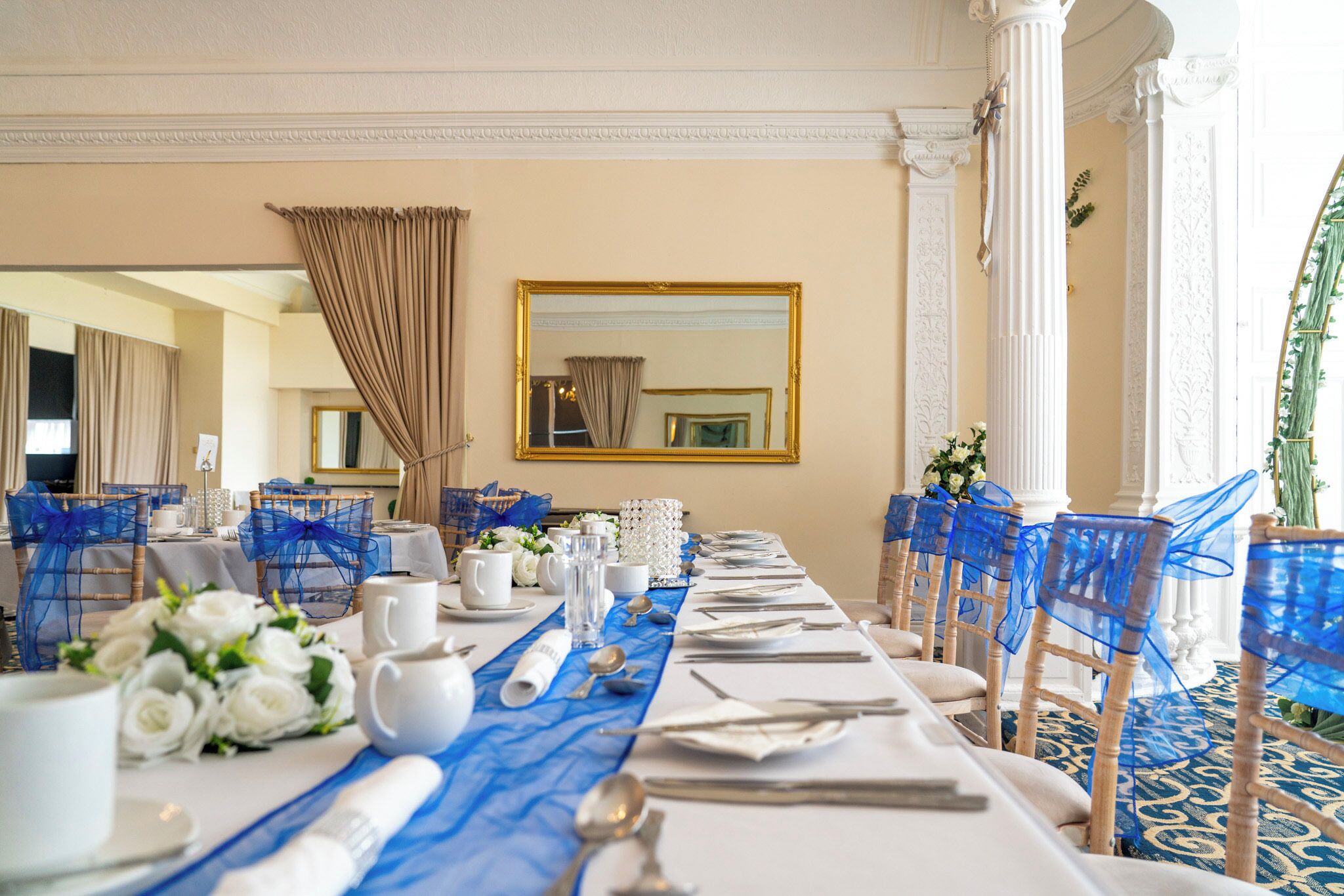 A long banquet table set with white tablecloths, blue chair covers, and white floral centerpieces.