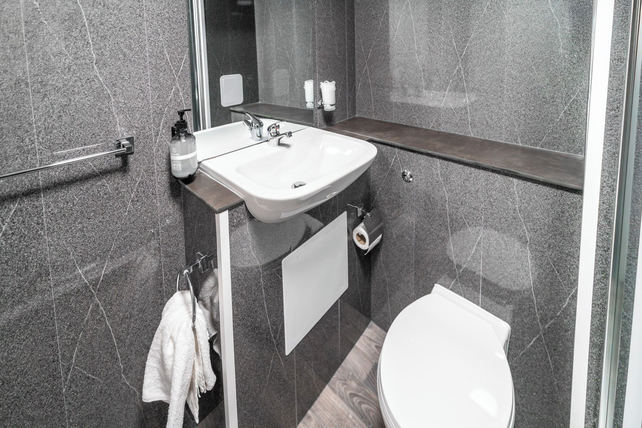 Un bagno moderno con un lavandino bianco, uno specchio, un portasciugamani e un water.