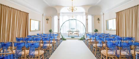 Un espace événementiel formel, avec des rangées de chaises, une allée centrale et une arche décorative.
