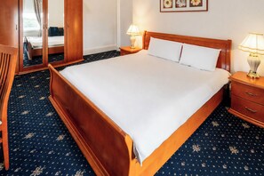 A hotel room with a large bed, wooden headboard, two bedside tables with lamps, a mirror, and a patterned carpet. - Adamton Country House Hotel (Prestwick)
