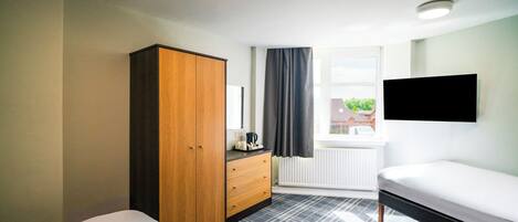 Un dormitorio con cama, armario, cómoda, espejo, ventana con cortinas y radiador.