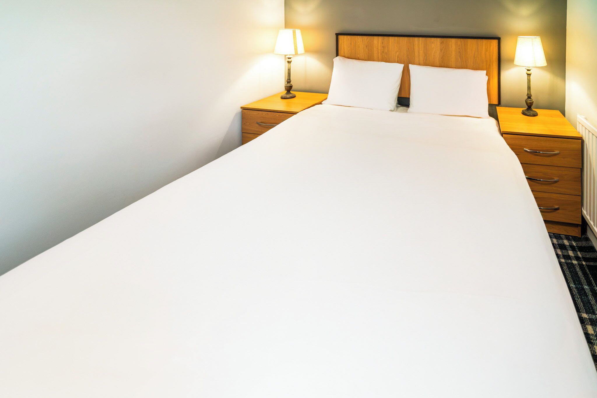 A single bed with white linens, two bedside tables with lamps, and a wooden headboard.