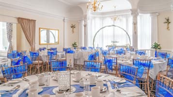 A banquet hall with round tables, blue chair covers, and white tablecloths.
