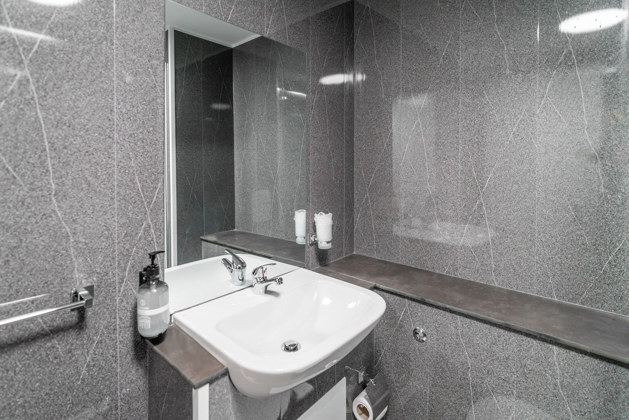 A modern bathroom with a white sink, a mirror, and a towel dispenser.
