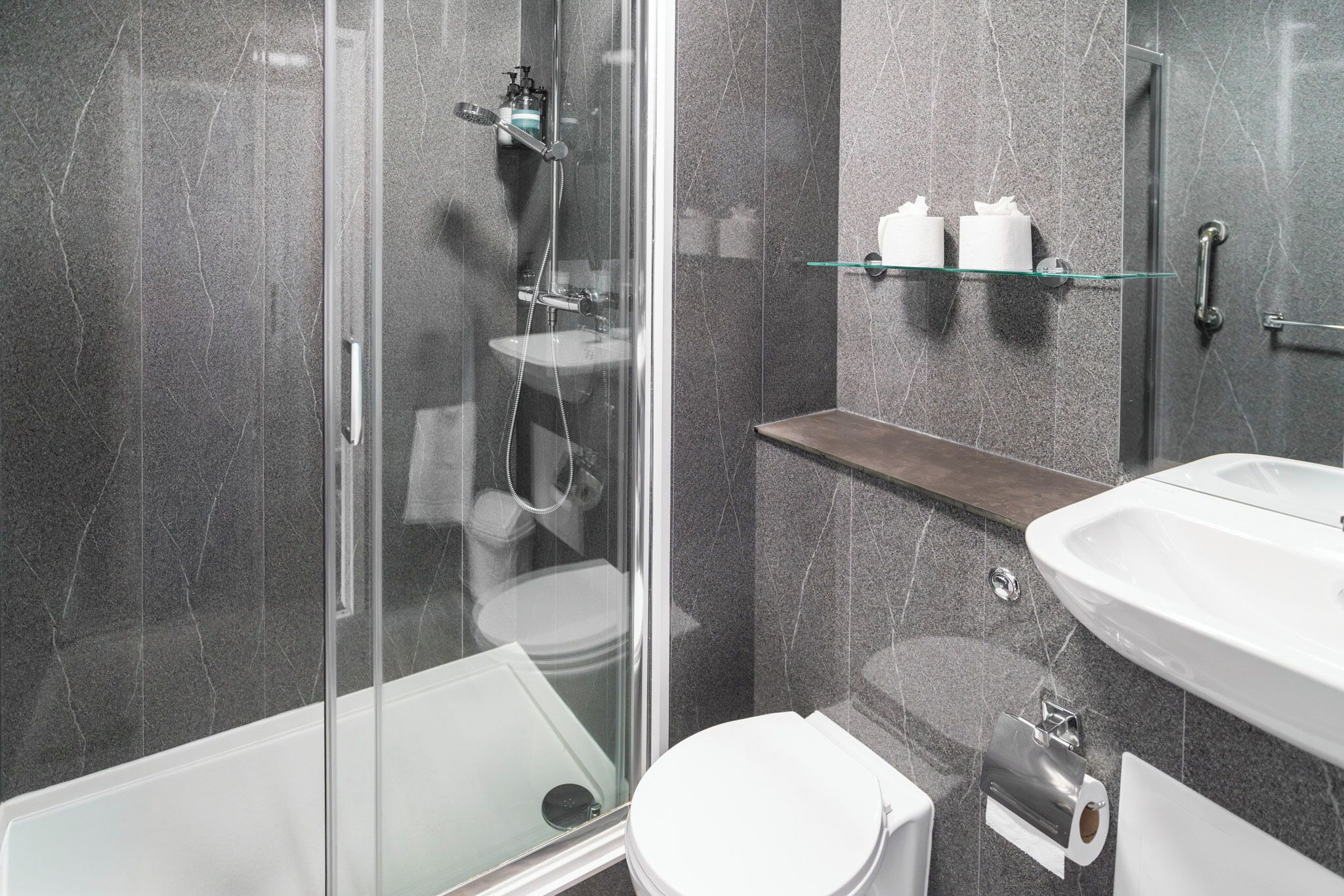 Ein modernes Badezimmer mit Duschkabine aus Glas, einem weißen Waschbecken und einer Toilette.