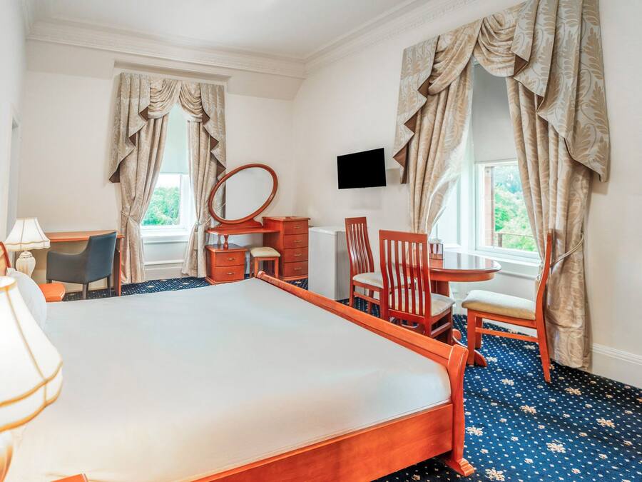 Een hotelkamer met een groot bed, een bureau met stoel, een dressoir, een spiegel en een televisie aan de muur.