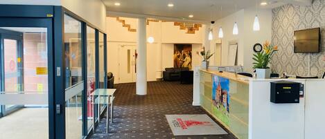 Zona de recepción de un hotel, con mostrador de recepción, área de estar y una escalera que conduce a otro piso.