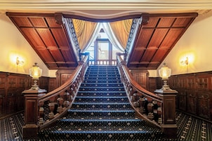 Una imponente escalera con barandales ornamentales y alfombra estampada, que conduce a un espacio interior luminoso.