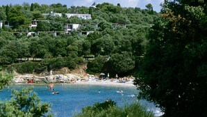 A coastal area with a beach, people swimming, and buildings on a hillside. - Horizont Resort (Pula)
