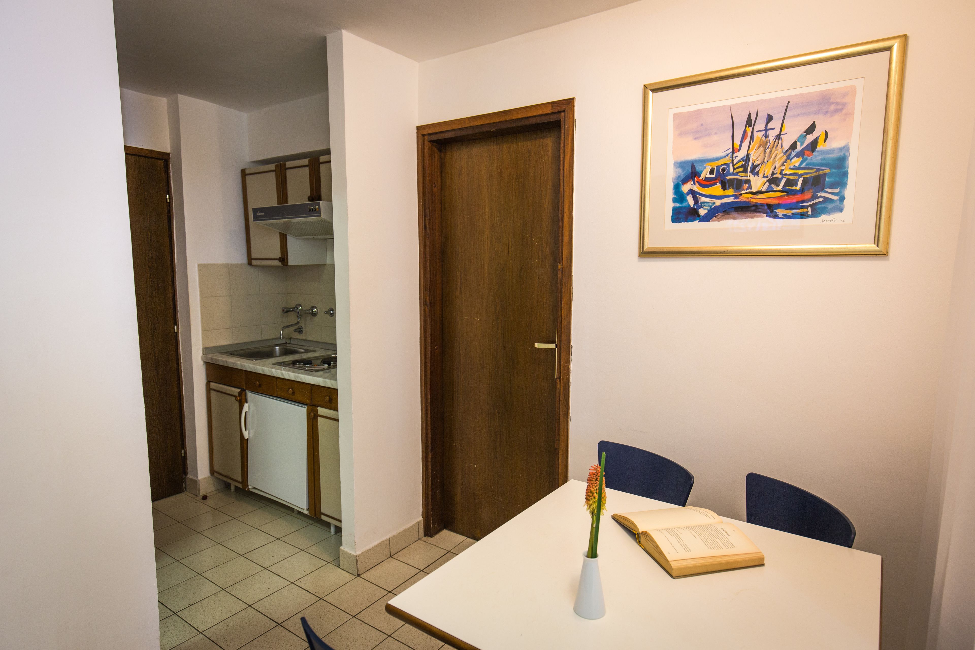 Une cuisine de taille réduite comprenant un coin repas, une porte et un tableau encadré accroché au mur.