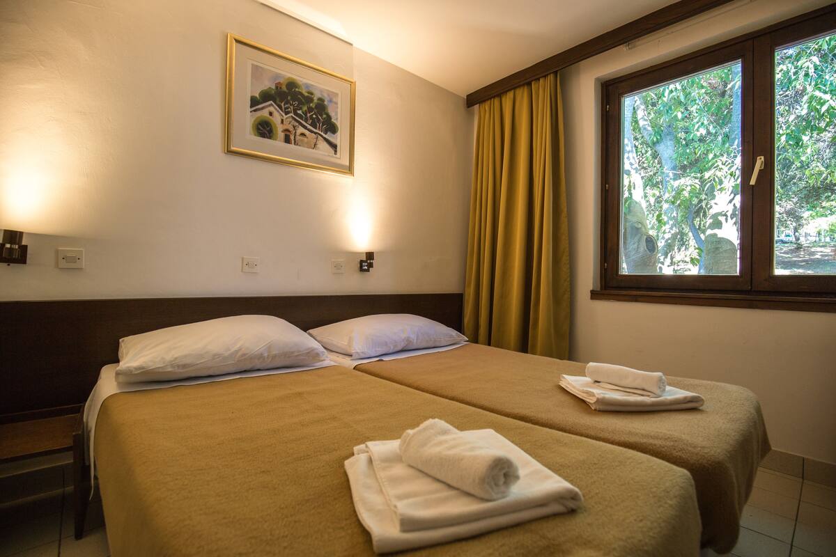A hotel room with two beds, a framed picture on the wall, and a window with curtains.