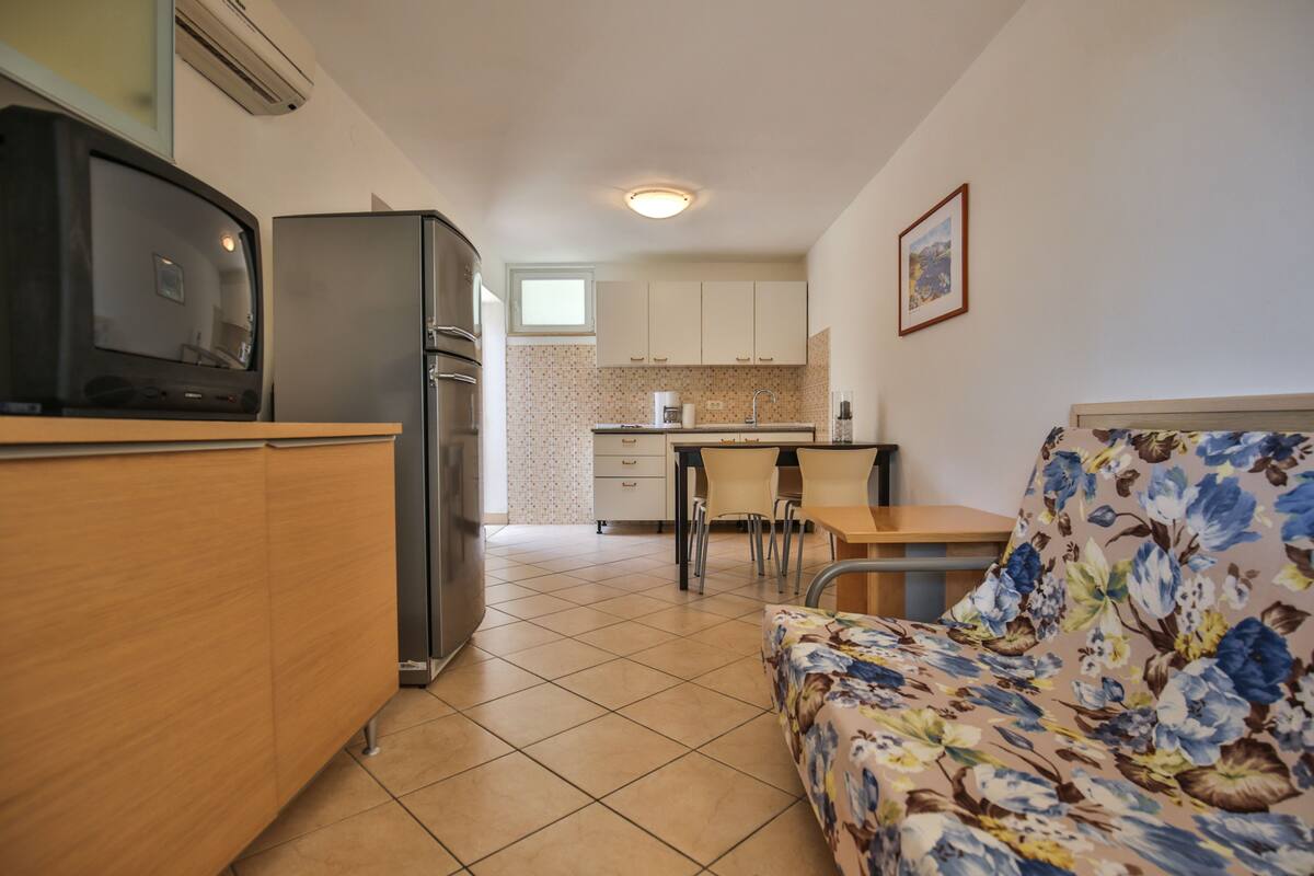 A compact kitchen with a refrigerator, microwave, and a dining area with a floral sofa and table.