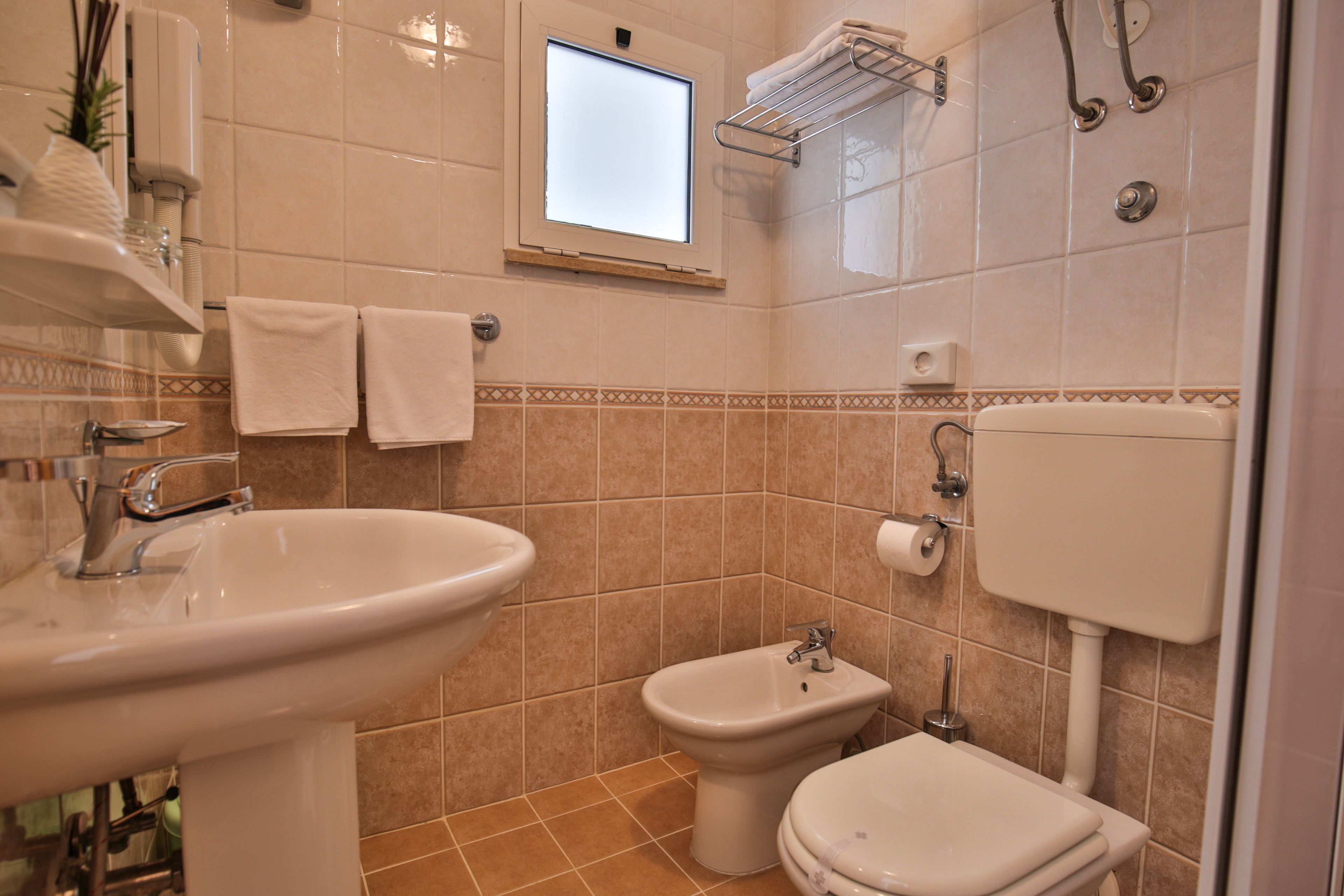 A bathroom with a sink, bidet, toilet, and a window.