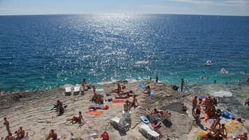 Una playa con gente tomando el sol y nadando, terreno rocoso y agua azul cristalina.