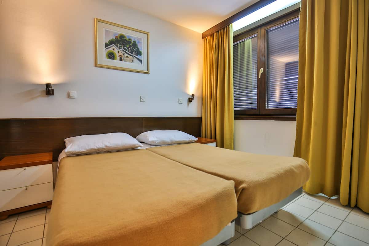 A double bed with two pillows, a nightstand, a framed picture on the wall, and a window with curtains.