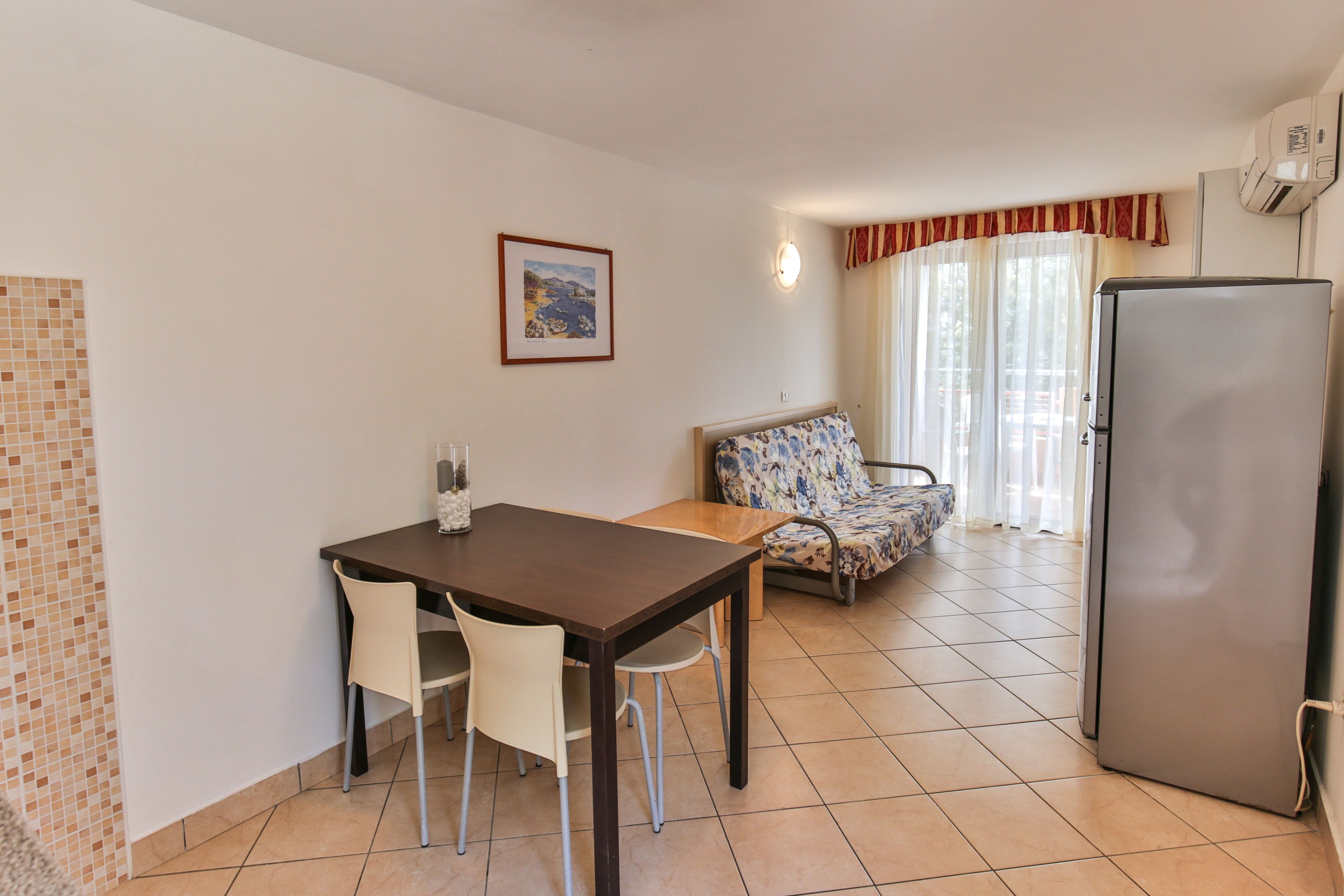 A small, clean room with a dining table, two chairs, a sofa, and a refrigerator.