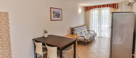 Una habitación pequeña y limpia con una mesa de comedor, dos sillas, un sofá y un refrigerador.