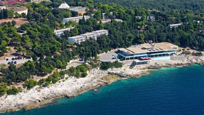 An aerial view of a coastal property with a large building, a rocky shoreline, and a clear blue sea. - Horizont Resort (Pula)