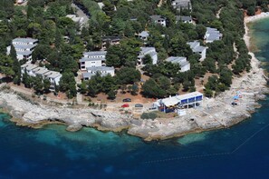 An aerial view of a coastal residential area with houses, a rocky shoreline, and clear blue waters.
