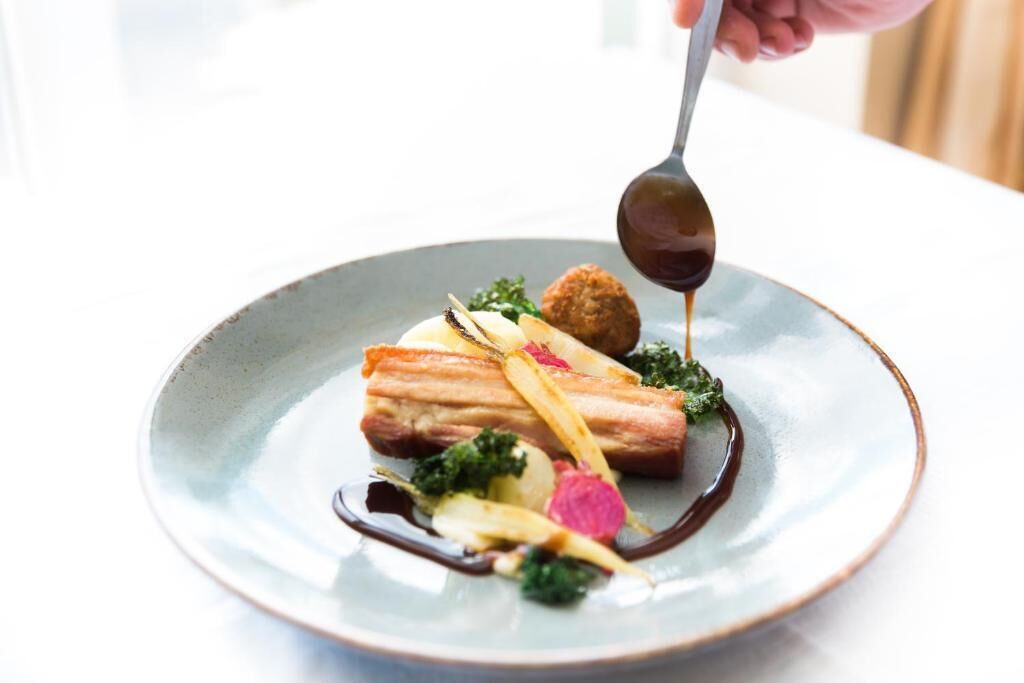 A plate of food with a spoonful of sauce being poured onto it.