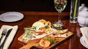Un plato de mariscos sobre una tabla de madera, con una copa de vino blanco, un recipiente pequeño de salsa y un salero en una mesa de madera.