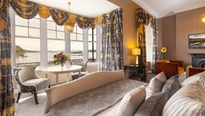 A hotel room with a large bed, a sitting area with a table and chairs, a fireplace, and large windows with curtains. - Eccles Hotel Glengarriff (Glengarriff)