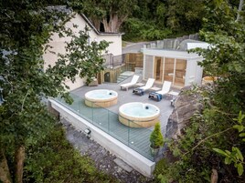 Terraza en la azotea con dos jacuzzis, sillas de descanso y barandilla de cristal.