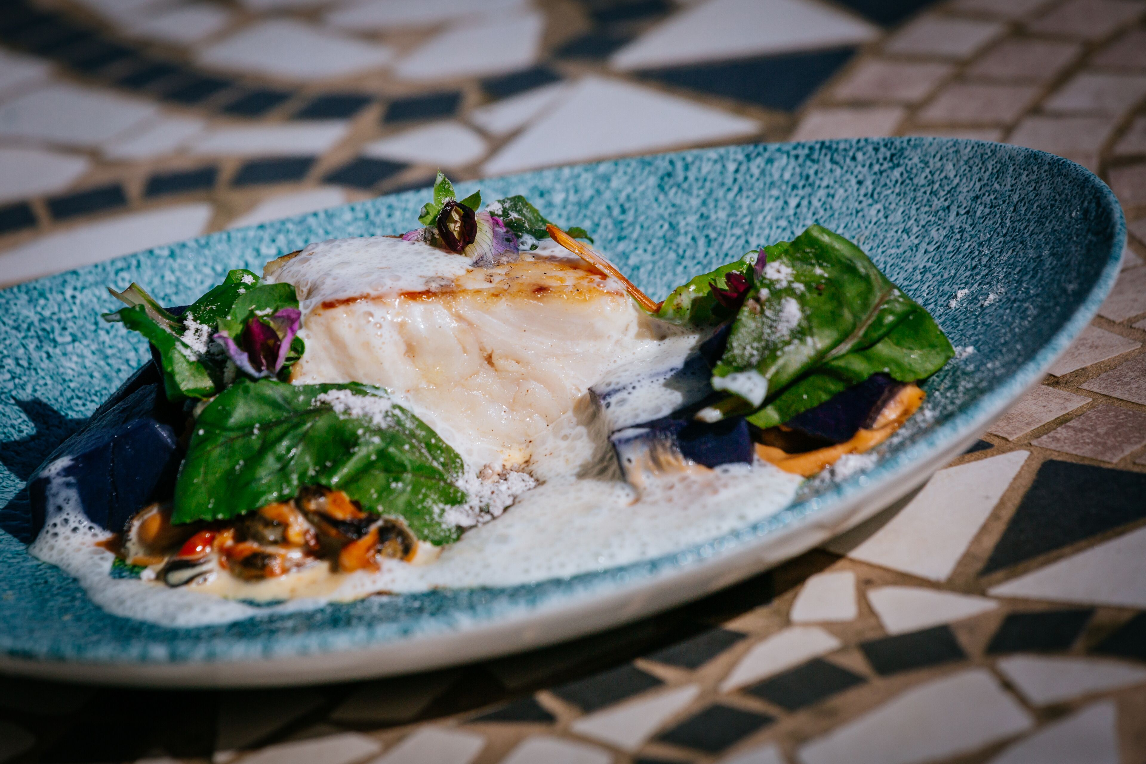 Un plato de comida con un filete de pescado blanco, verduras y salsa cremosa sobre un plato azul.