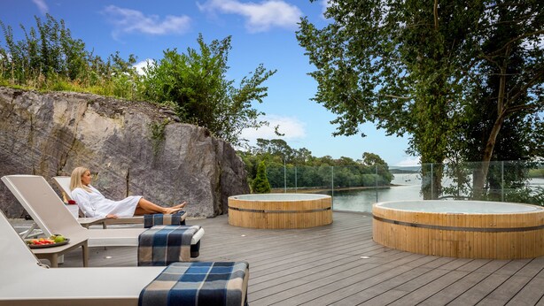 A wooden deck with lounge chairs and a hot tub, overlooking a body of water and greenery. - Eccles Hotel Glengarriff (Glengarriff)