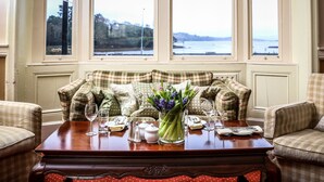 A cozy room with a checkered sofa, a wooden coffee table, and a view of a body of water through large windows. - Eccles Hotel Glengarriff (Glengarriff)