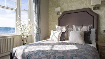 A bedroom with a large bed, a view of the sea through a window, and a vase with flowers.