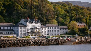 A waterfront hotel with multiple buildings, a stone pier, and a forested hillside in the background. - Eccles Hotel Glengarriff (Glengarriff)