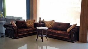 A modern living room with a dark brown sectional sofa, a small round table, and a grey sofa in the background. - Divine the Boutique Hotel (Jaipur)