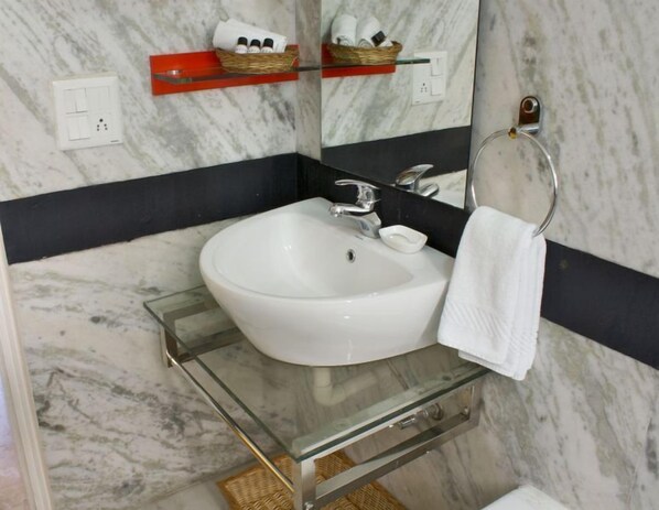 Un baño con lavamanos blanco, encimera de cristal, espejo y argolla para toallas.