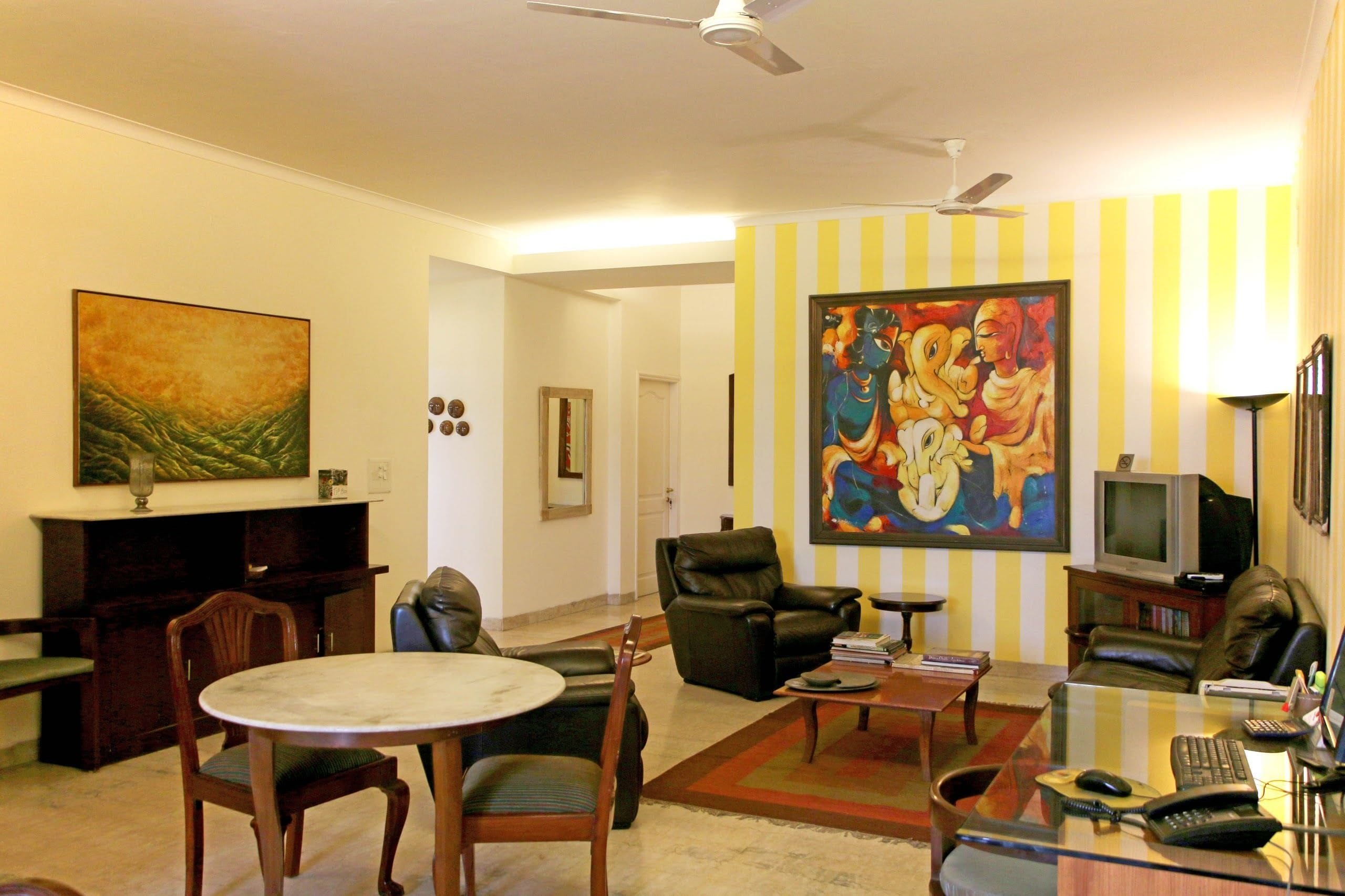 A living room with a round table, leather chairs, a television, and a large painting on the wall.