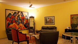 Una sala de estar con un cuadro grande, un sofá, una silla, una mesa y un ventilador de techo.