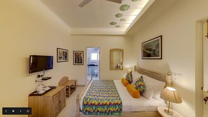 Habitación de hotel con cama, televisión, escritorio y baño visible a través de una puerta abierta.