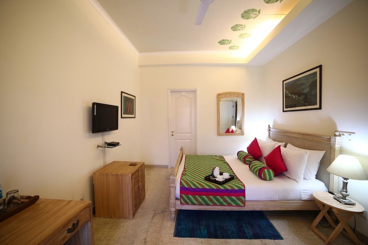 A bedroom with a bed, a television, a mirror, a door, and a small wooden cabinet.