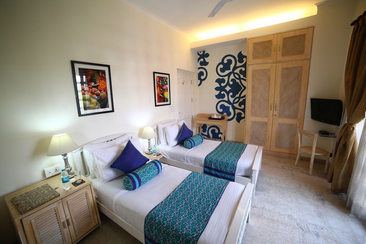 Habitación de hotel con dos camas, un armario, un televisor y obras de arte en las paredes.