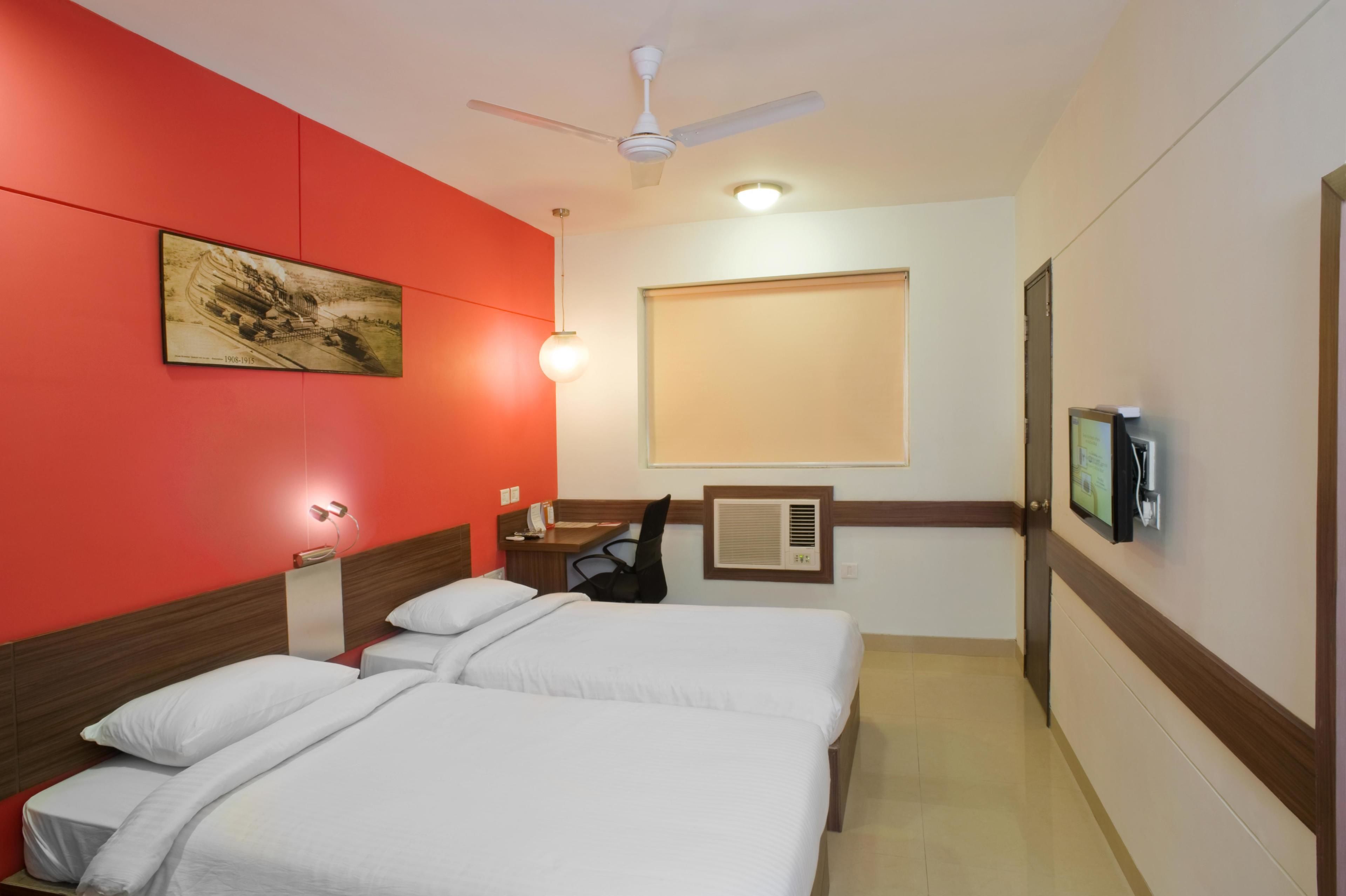 A hotel room with two beds, a ceiling fan, a mounted TV, and a window with blinds.